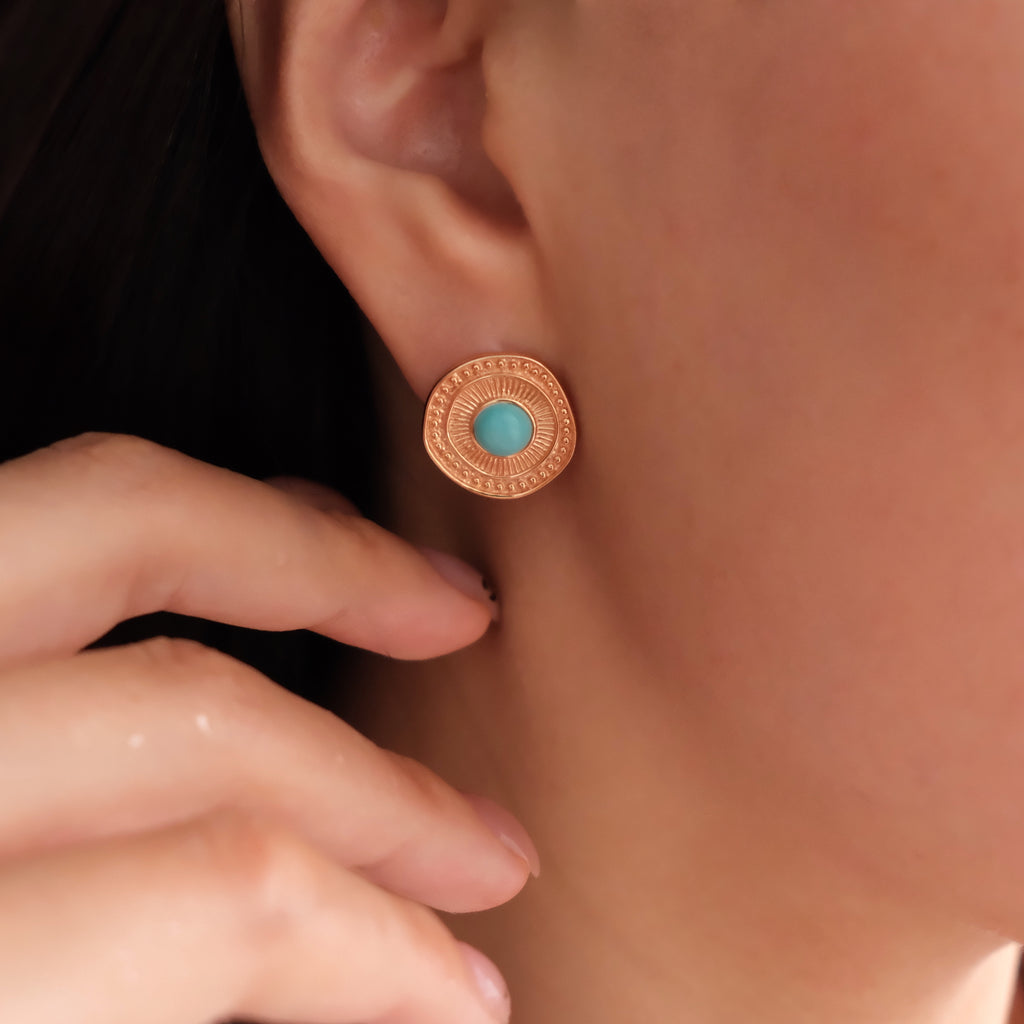 Close-up of a person wearing a gold earring with a turquoise stone.