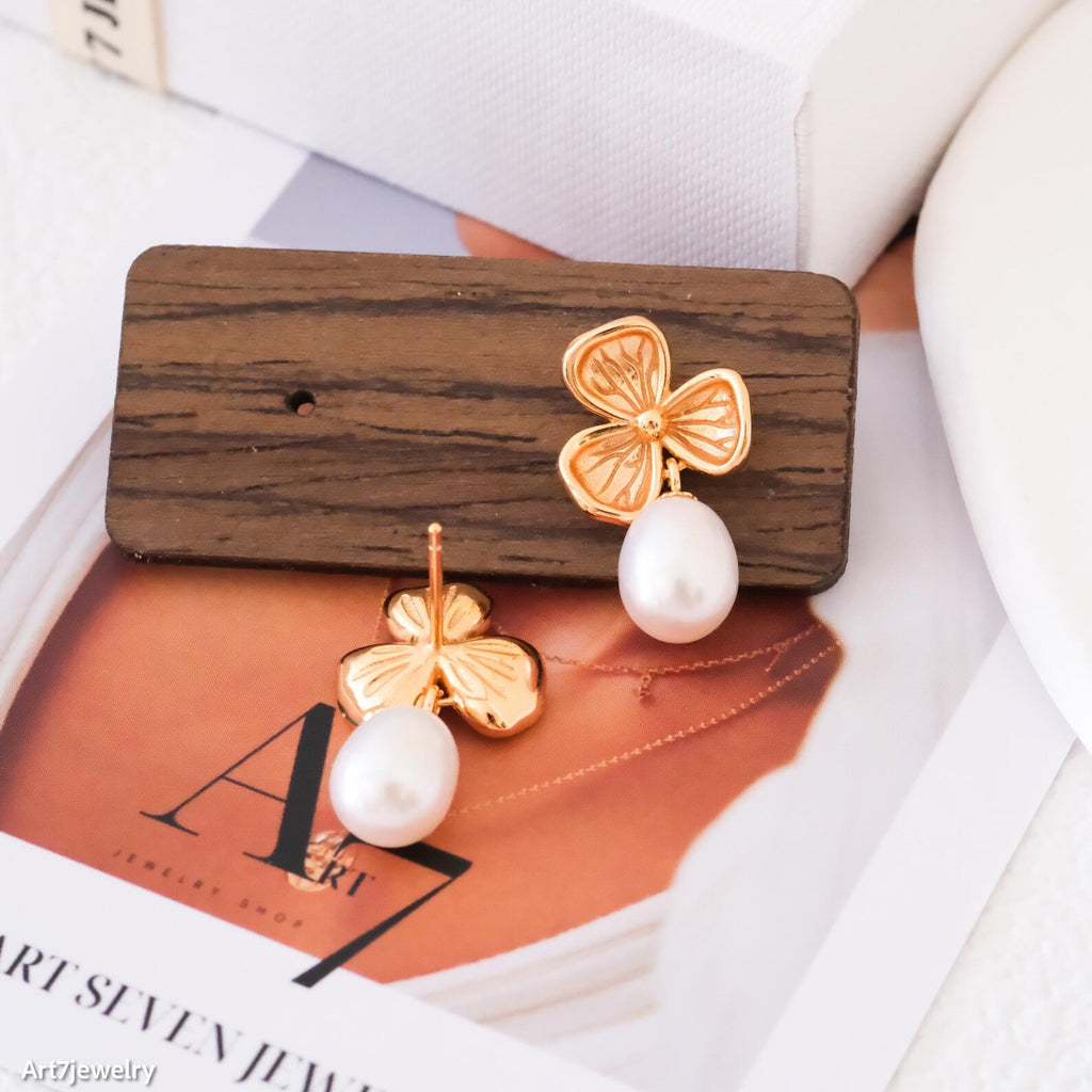 Gold four-leaf clover earrings with white pearls on a wooden stand.