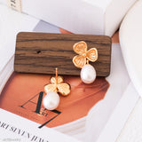 Gold four-leaf clover earrings with white pearls on a wooden stand.