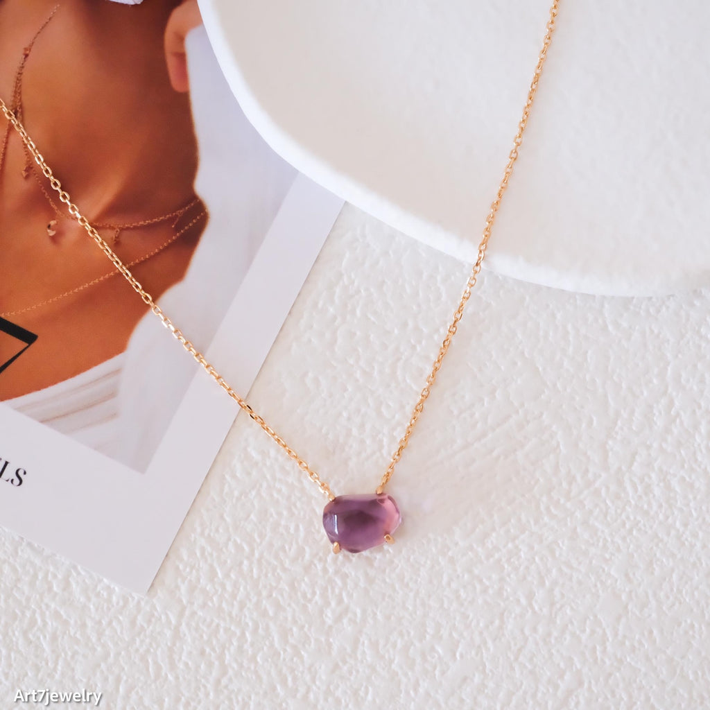 Necklace with a purple gemstone on a textured white surface