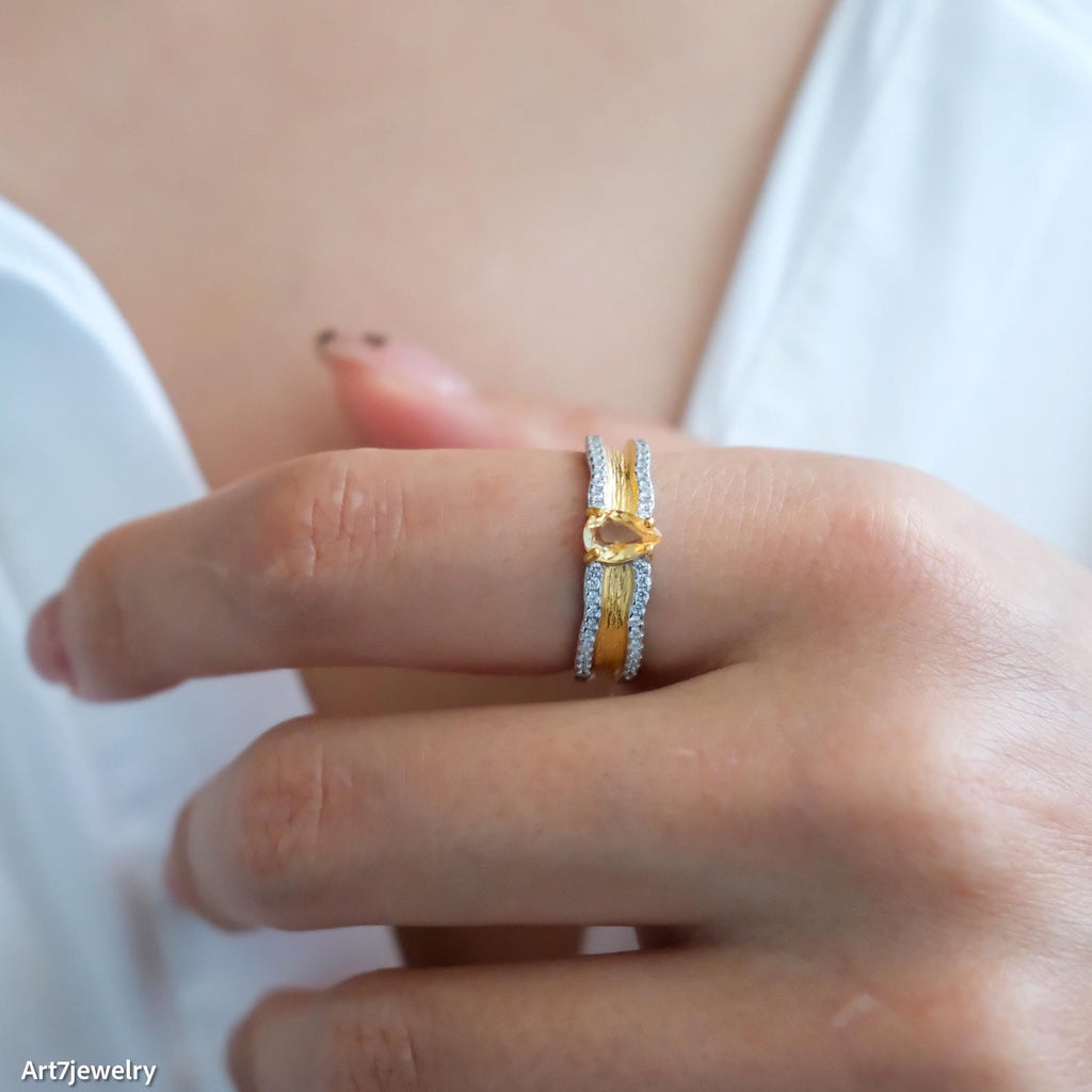 Gold ring with a yellow gemstone on a person's finger against a white background