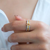 Gold ring with a yellow gemstone on a person's finger against a white background