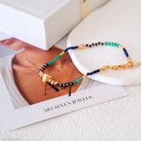Green and blue beaded bracelets on a magazine with 'Art Seven Jewels' branding.