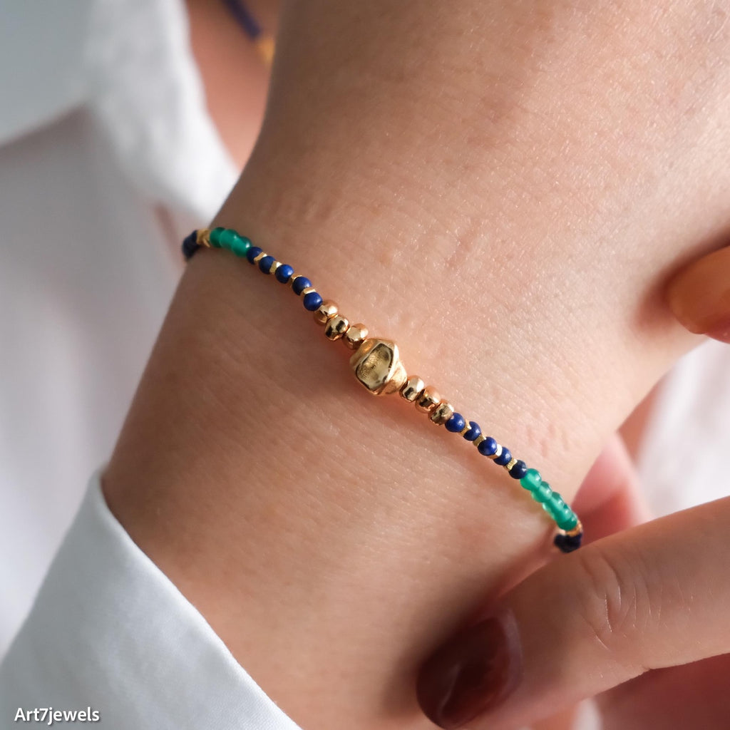 Close-up of a hand wearing a beaded bracelet with green, blue, and gold beads.