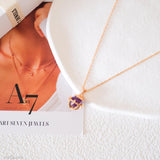 Gold necklace with a purple pendant on a white surface, with 'Ari Seven Jewels' branding.