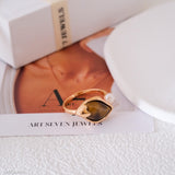 Gold ring with a heart-shaped gemstone and pearl on Art Seven Jewels packaging.