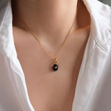 Gold necklace with a black pendant on a mannequin wearing a white shirt.