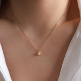 Gold necklace with a small pendant on a person wearing a white top.