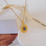 Gold sapphire pendant necklace with natural blue sapphire center stone, surrounded by small sparkling accents on a textured round gold disc, delicate minimalist chain jewelry for women
