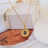 Gold sapphire pendant necklace with natural blue sapphire center stone, surrounded by small sparkling accents on a textured round gold disc, delicate minimalist chain jewelry for women