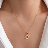 Gold sapphire pendant necklace with natural blue sapphire center stone, surrounded by small sparkling accents on a textured round gold disc, delicate minimalist chain jewelry for women