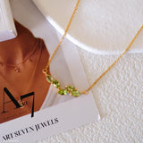 Natural peridot necklace featuring five genuine marquise-cut green peridot gemstones in a delicate curved gold bar design on a fine gold chain, elegant August birthstone jewelry for women.