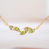 Natural peridot necklace featuring five genuine marquise-cut green peridot gemstones in a delicate curved gold bar design on a fine gold chain, elegant August birthstone jewelry for women.