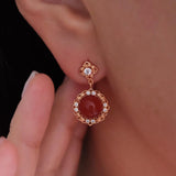 Natural carnelian dangle earrings with polished red carnelian cabochons, gold-tone filigree settings, and clear crystal accents.