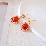 Natural carnelian dangle earrings with polished red carnelian cabochons, gold-tone filigree settings, and clear crystal accents.
