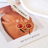 Natural carnelian dangle earrings with polished red carnelian cabochons, gold-tone filigree settings, and clear crystal accents.