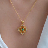 Natural emerald clover pendant necklace with a green emerald center, gold-tone openwork radiating lines, and clear crystal accents.