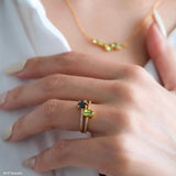 Oval green peridot solitaire ring in a gold-tone four-prong setting with sparkling clear stone band accents.