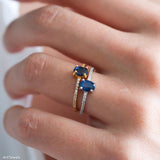 Blue sapphire solitaire ring with an oval deep-blue center stone, silver-tone four-prong setting, and a slim clear stone accent band.