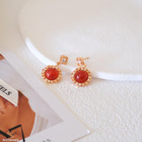 Natural carnelian dangle earrings with polished red carnelian cabochons, gold-tone filigree settings, and clear crystal accents.