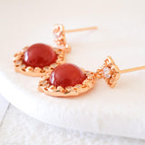 Natural carnelian dangle earrings with polished red carnelian cabochons, gold-tone filigree settings, and clear crystal accents.