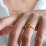 Oval green peridot solitaire ring in a gold-tone four-prong setting with sparkling clear stone band accents.