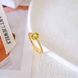 Oval green peridot solitaire ring in a gold-tone four-prong setting with sparkling clear stone band accents.
