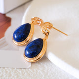 Pair of natural lapis lazuli teardrop drop earrings in 18K gold bezel setting with geometric filigree studs on white stone background by Art7Jewels