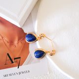 Close-up of blue gemstone teardrop earrings featuring 18K gold cutout filigree detailing and post back closure