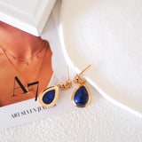 Close-up of blue gemstone teardrop earrings featuring 18K gold cutout filigree detailing and post back closure