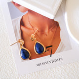 Close-up of blue gemstone teardrop earrings featuring 18K gold cutout filigree detailing and post back closure