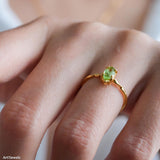 Olive-green marquise peridot ring in a gold-tone prong setting with a delicate wave-style band.