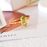 Olive-green marquise peridot ring in a gold-tone prong setting with a delicate wave-style band.