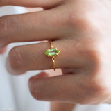 Olive-green marquise peridot ring in a gold-tone prong setting with a delicate wave-style band.