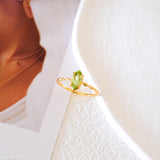 Olive-green marquise peridot ring in a gold-tone prong setting with a delicate wave-style band.