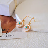 Gold-tone turquoise drop earrings with iridescent mother of pearl discs and detailed sunburst center accents.