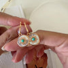 Gold-tone turquoise drop earrings with iridescent mother of pearl discs and detailed sunburst center accents.