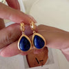 Close-up of blue gemstone teardrop earrings featuring 18K gold cutout filigree detailing and post back closure