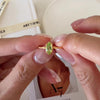 Olive-green marquise peridot ring in a gold-tone prong setting with a delicate wave-style band.